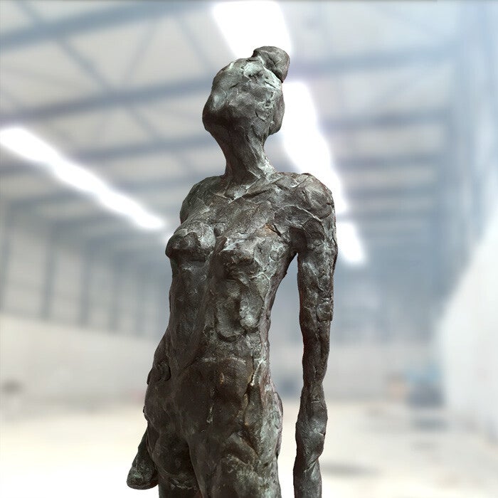 Het bovenlijf van een bronzen beeld van een vrouw met een hoge knot