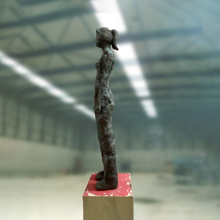 Een zijaanzicht van een bronzen beeld van een meisje met een paardenstaart op een houten sokkel
