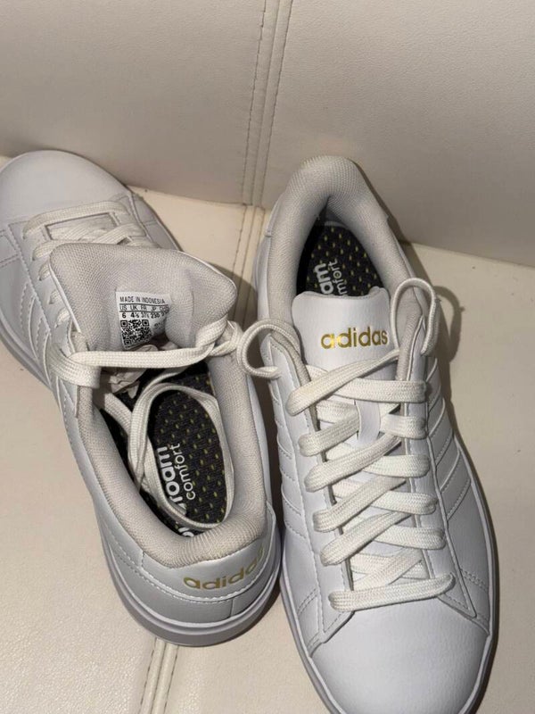 are white adidas Grand Court 2.0 sneakers featuring gold metallic branding and