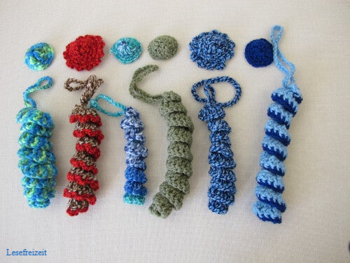 Die Körper von gehäkelten Glückswürmchen noch ohne Holzperle als Kopf sowie Mützen und Hüte.