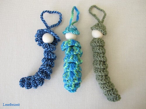 Drei fertig gehäkelte Glückswürmchen. Das Gesicht muss noch auf die Holzperle aufgemalt werden.