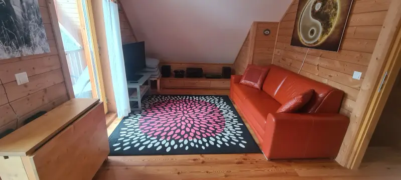 Die andere Seite des Schlafzimmers: Gemütliche TV-Lounge im Obergeschoss des Blockhaus Hengsttal mit rotem Ledersofa, modernem Teppich u mit einem Tisch der gerne als Arbeitsplatz verwendet wird.