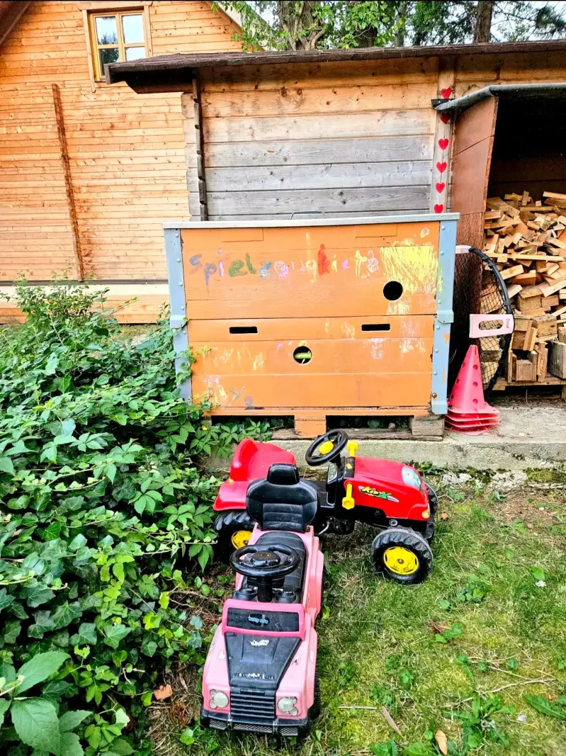  Große Spielzeugkiste im Außenbereich des Blockhaus Hengsttal mit bunten Kinderfahrzeugen wie Traktoren und Bobby-Cars für kleine Gäste.