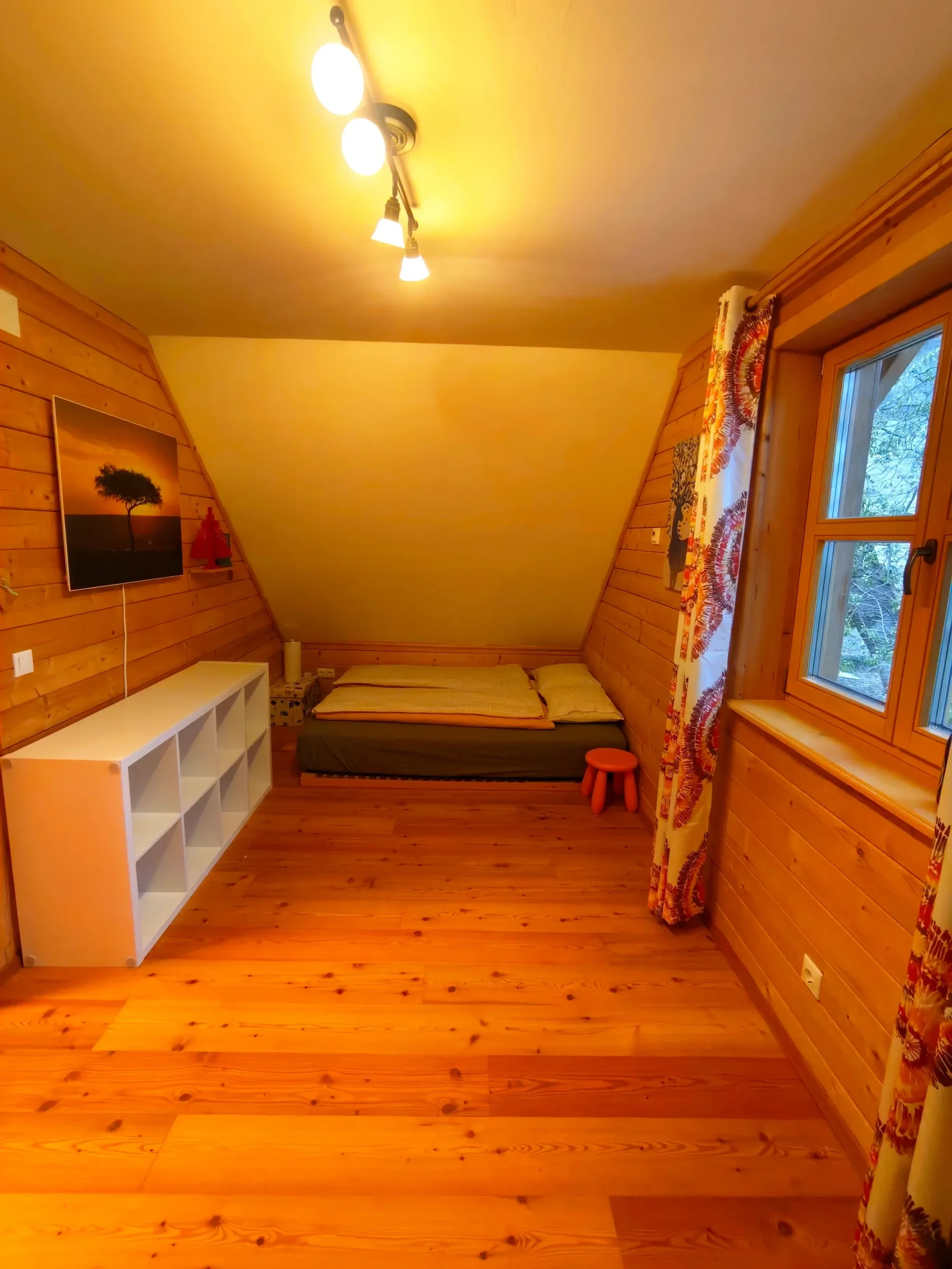 Zweites gemütliches Schlafzimmer im Dachgeschoss des Blockhaus Hengsttal mit Doppelbett, hellen Massivholzwänden und modernem weißen Regal. 