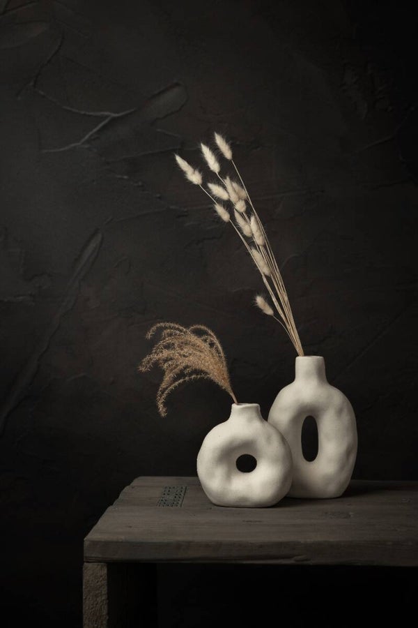 Donker stilleven met droogbloemen in witte organische donut vazen
