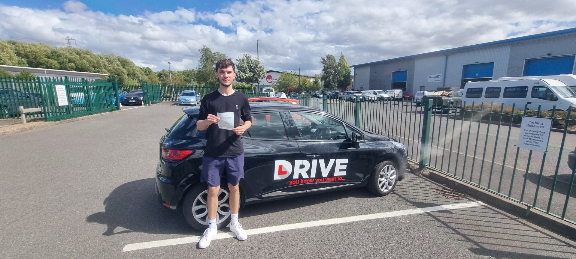 Happy driving school student holding a practical driving test pass certificate outside the tuition car.