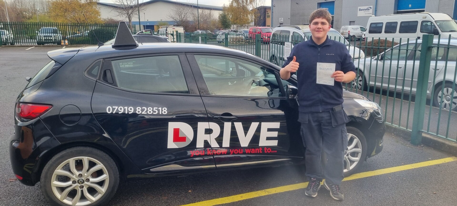 Happy driving school student holding a practical driving test pass certificate outside the tuition car.