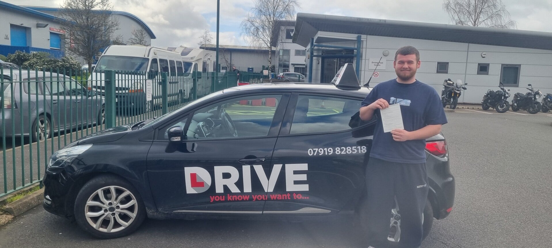 Happy driving school student holding a practical driving test pass certificate outside the tuition car.