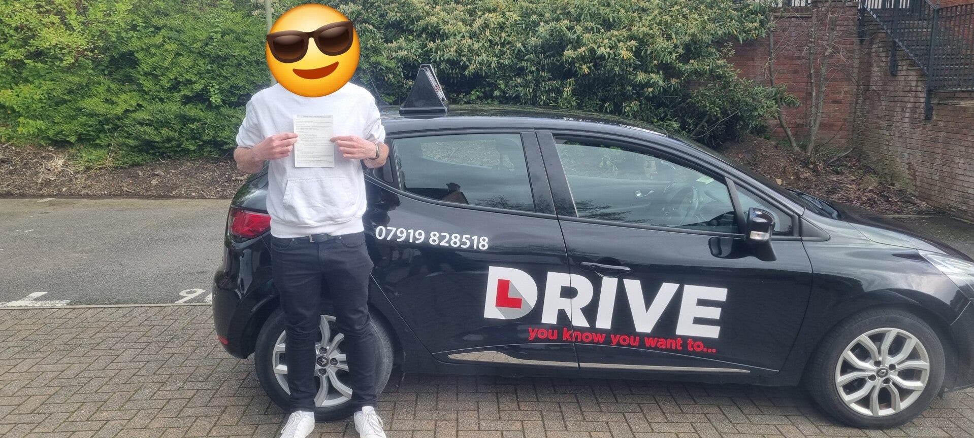 Happy driving school student holding a practical driving test pass certificate outside the tuition car.