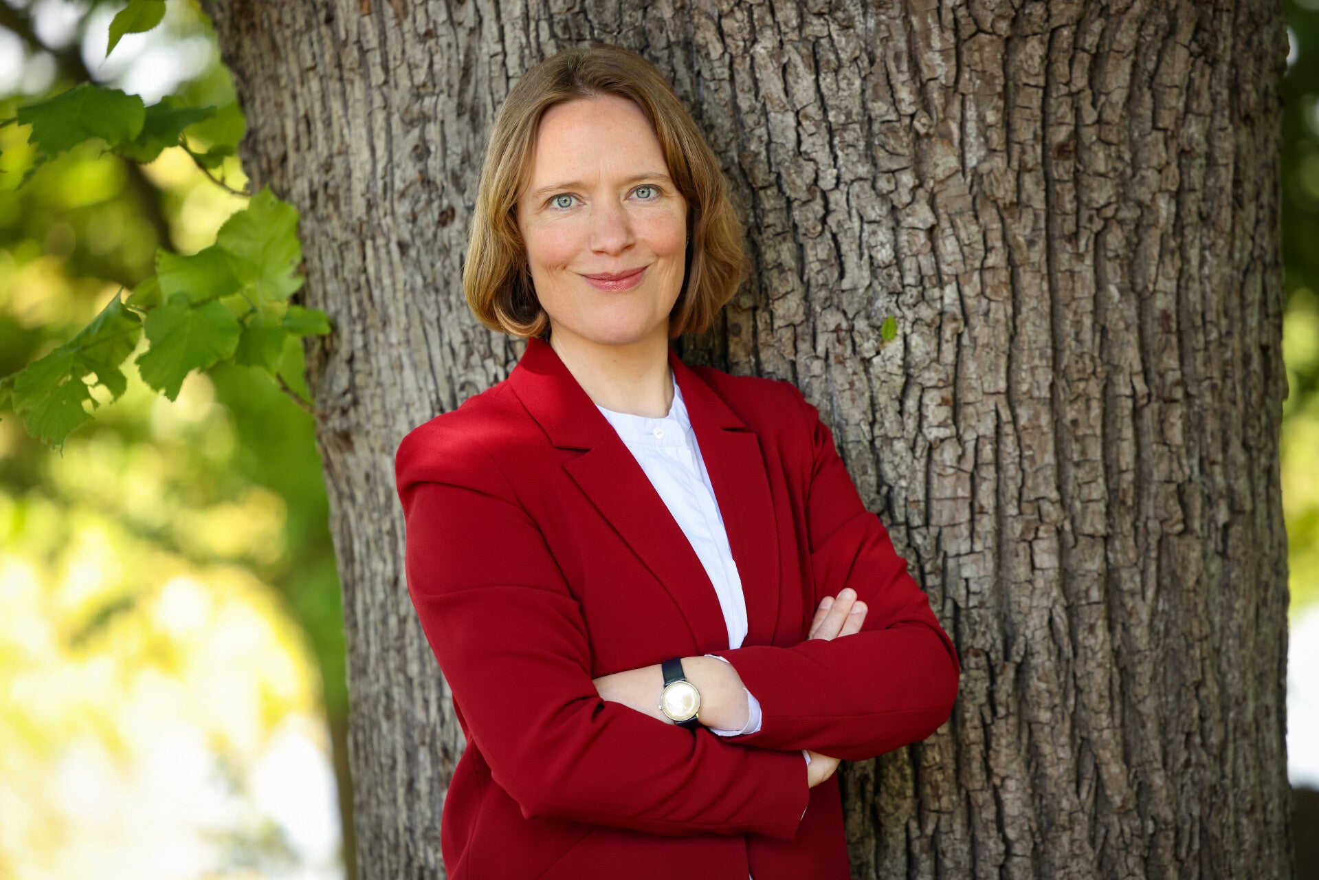 Stefanie Duensing möchte Ihre landrätin werden. Sie steht an eine weiße Holzwand gelehnt und lächelt offen.