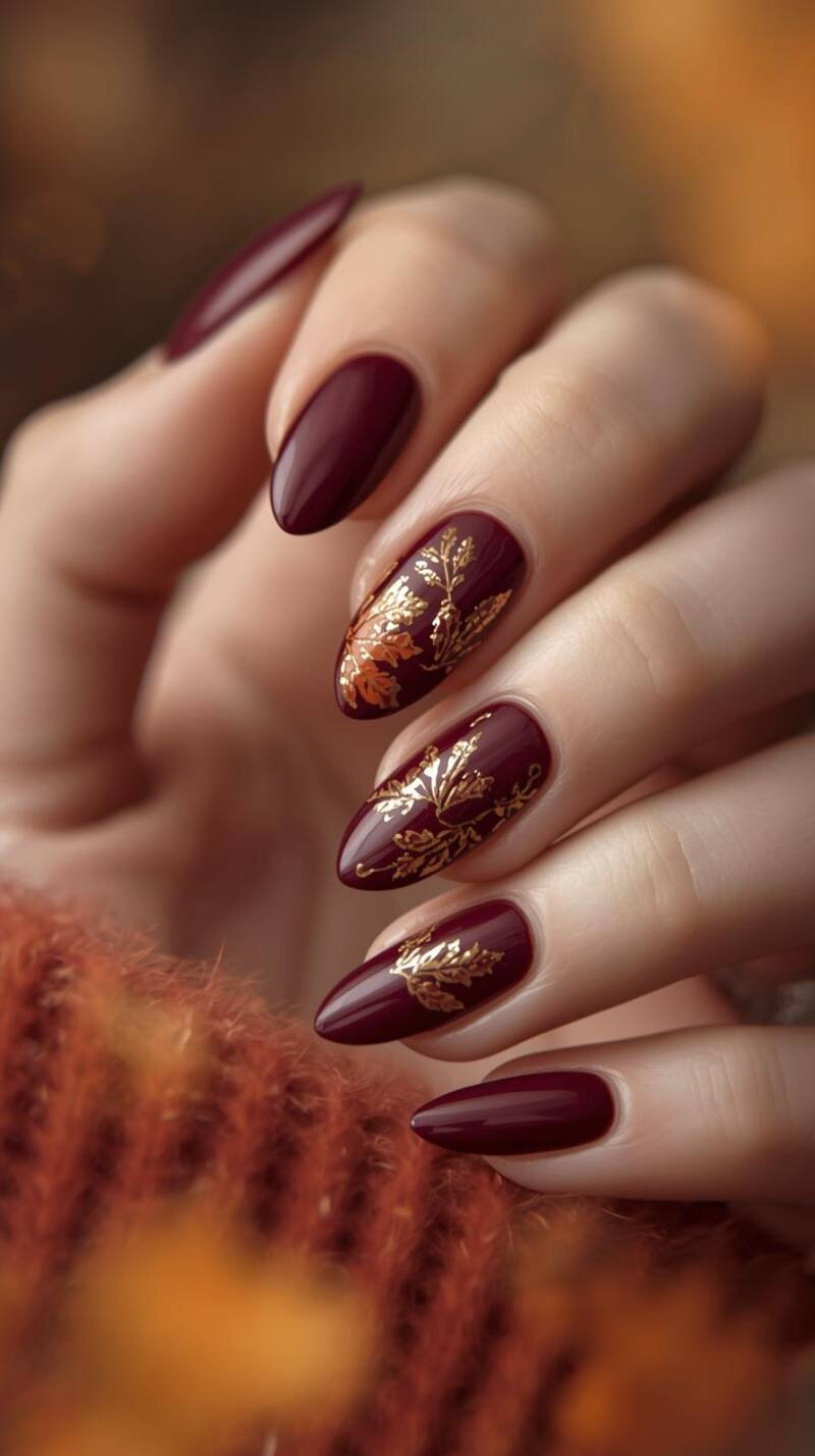 _a-realistic-close-up-of-a-female-hand-with-almond-shaped-nails-painted-in-deep-burgundy-with-golden-foil-accents-some-nails-feature-delicate-hand-painted-autumn-l-2-standard-p8srp9.jpg