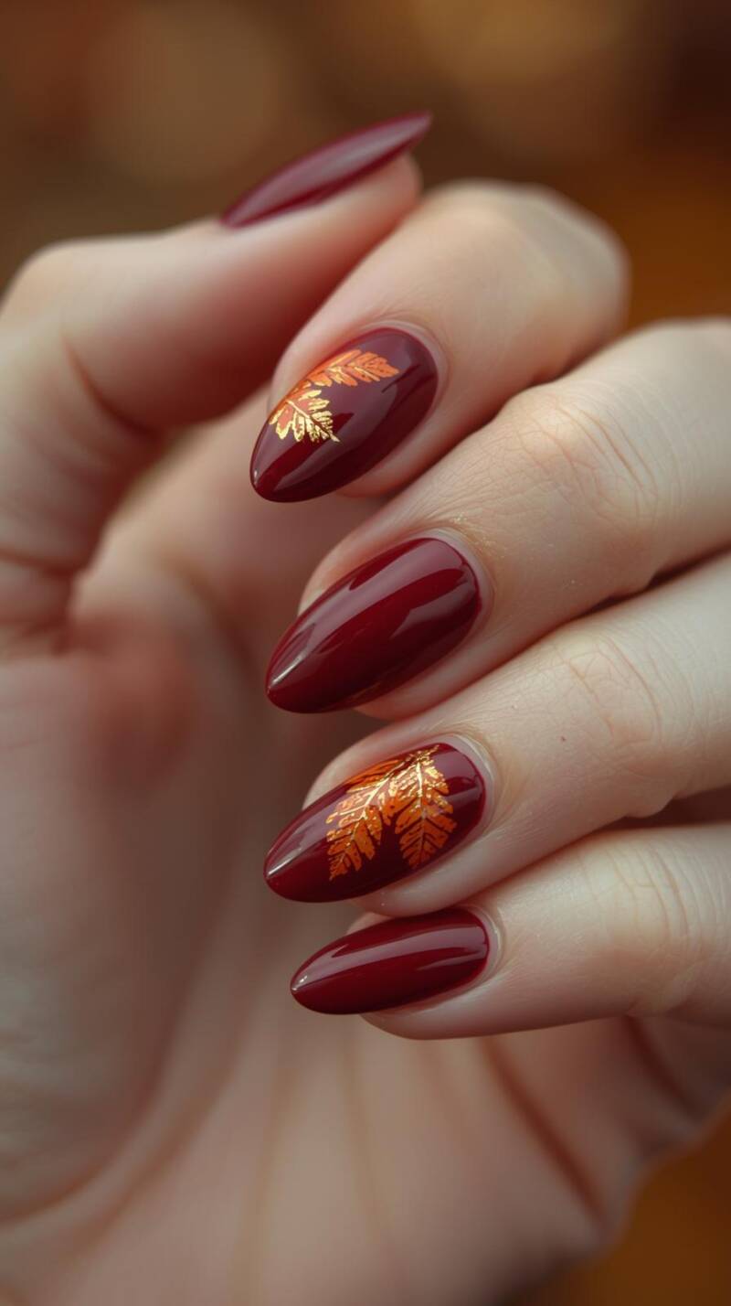 _a-realistic-close-up-of-a-female-hand-with-almond-shaped-nails-painted-in-deep-burgundy-with-golden-foil-accents-some-nails-feature-delicate-hand-painted-autumn-leave-standard-zyrid8.jpg