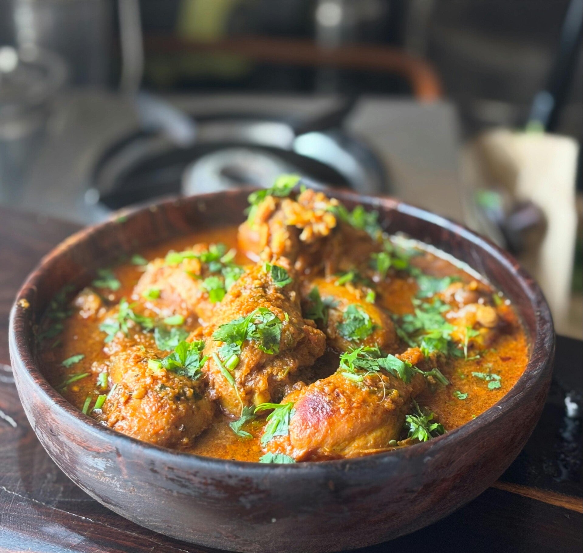 Ein würziges indisches Currygericht mit Hähnchen und frischen Kräutern in einer dunklen Schale.