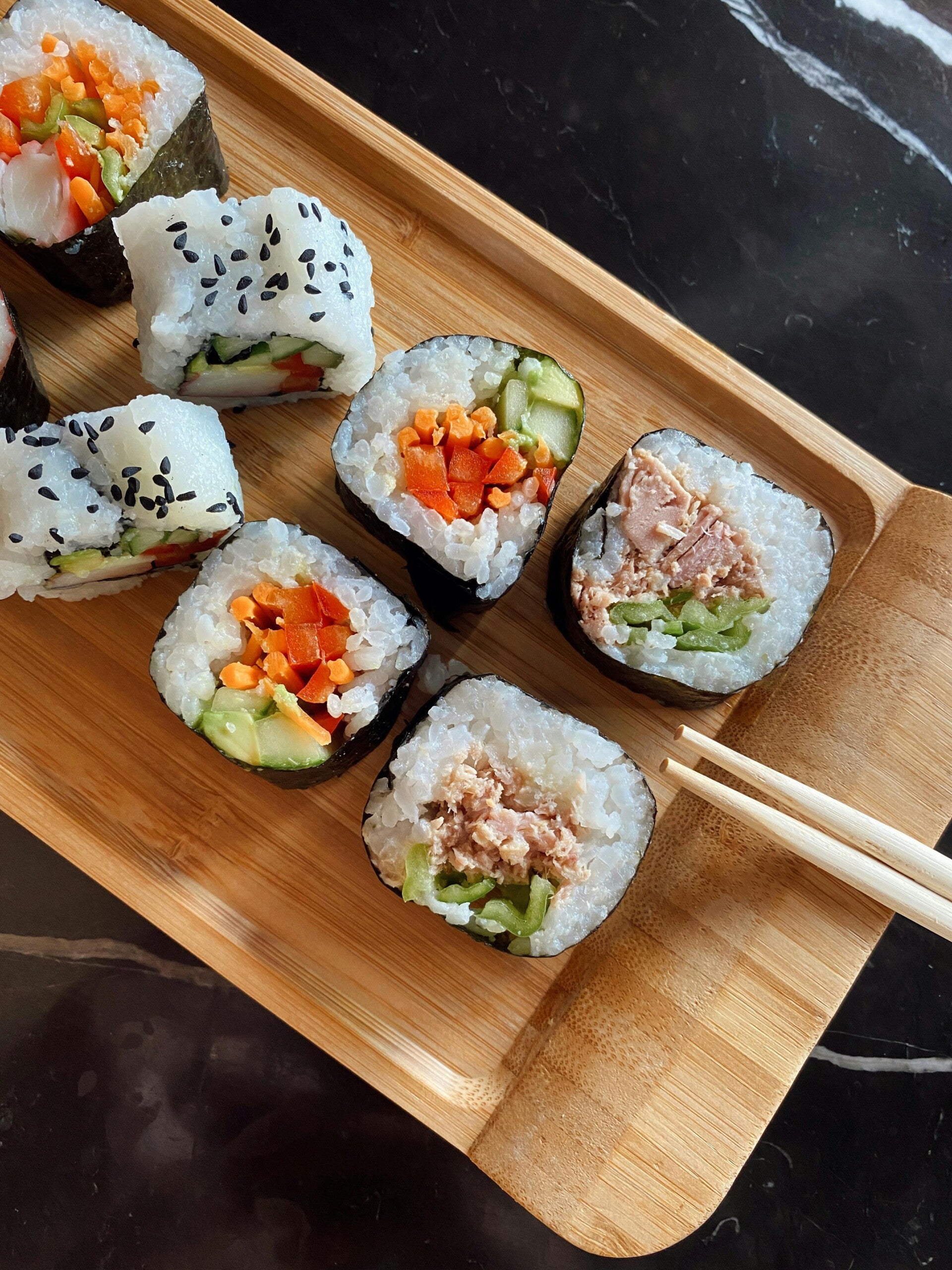 Eine Auswahl frisch zubereiteter Sushi-Rollen mit Gemüse und Thunfisch sowie Holzstäbchen auf einer Servierplatte.