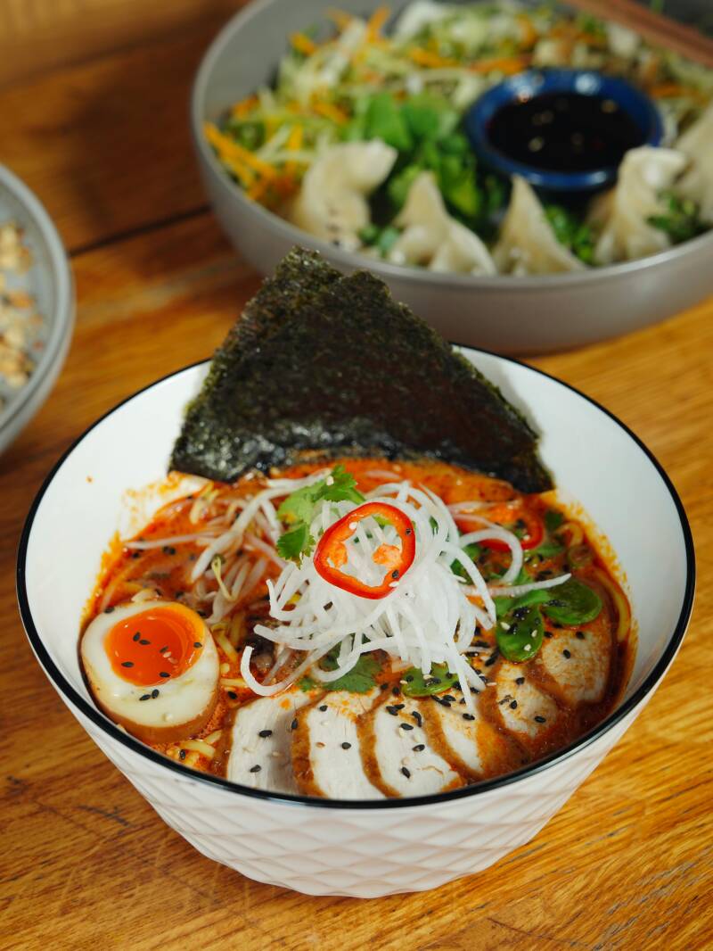 Eine Schale japanische Ramen-Suppe mit Nudeln, einem halbierten Ei, Frühlingszwiebeln und Nori-Algenblatt.