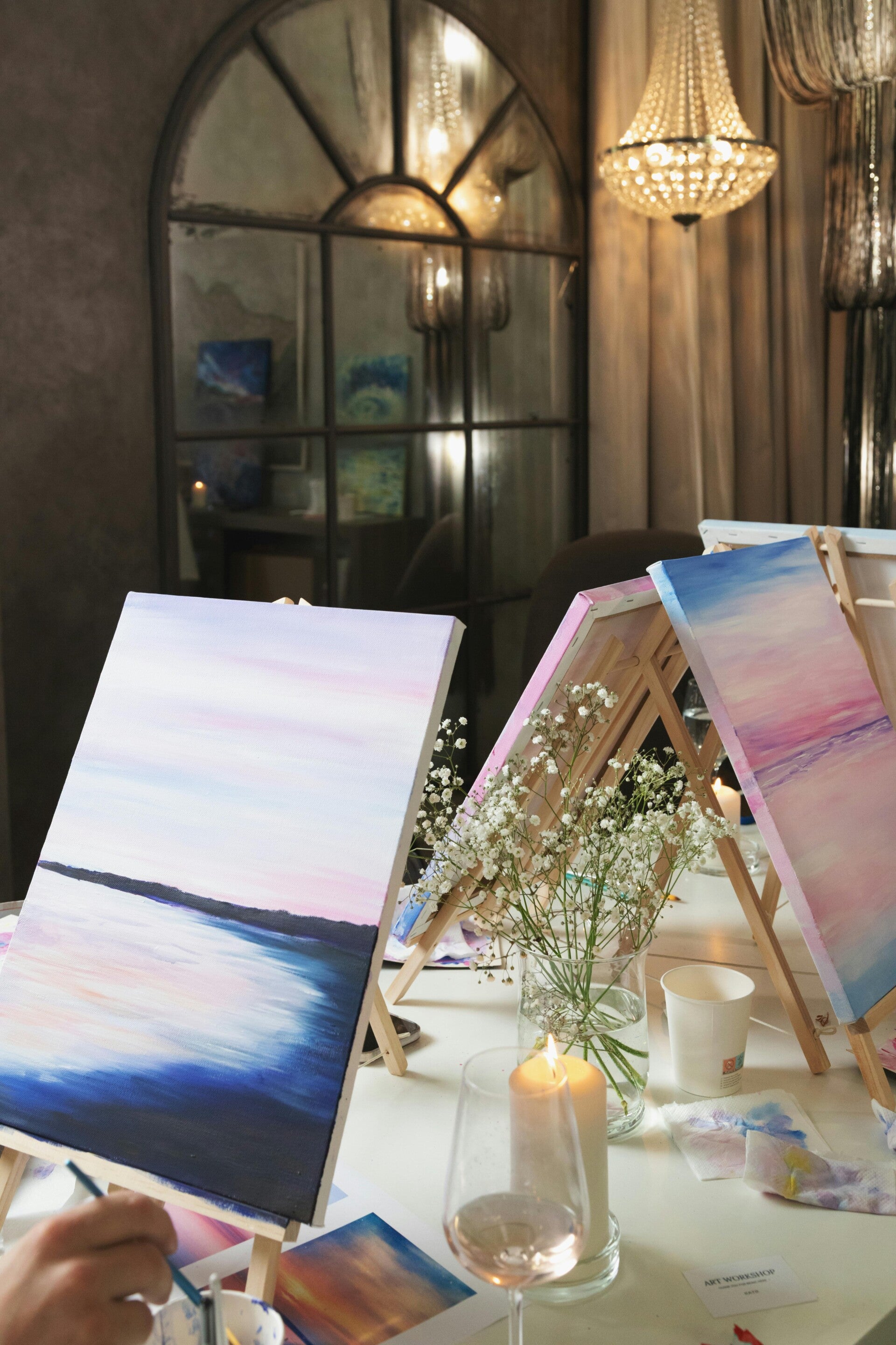 Mehrere Staffeleien mit bunten Leinwänden, Pinseln und Weingläsern stehen für ein Sip und Paint Event bereit.