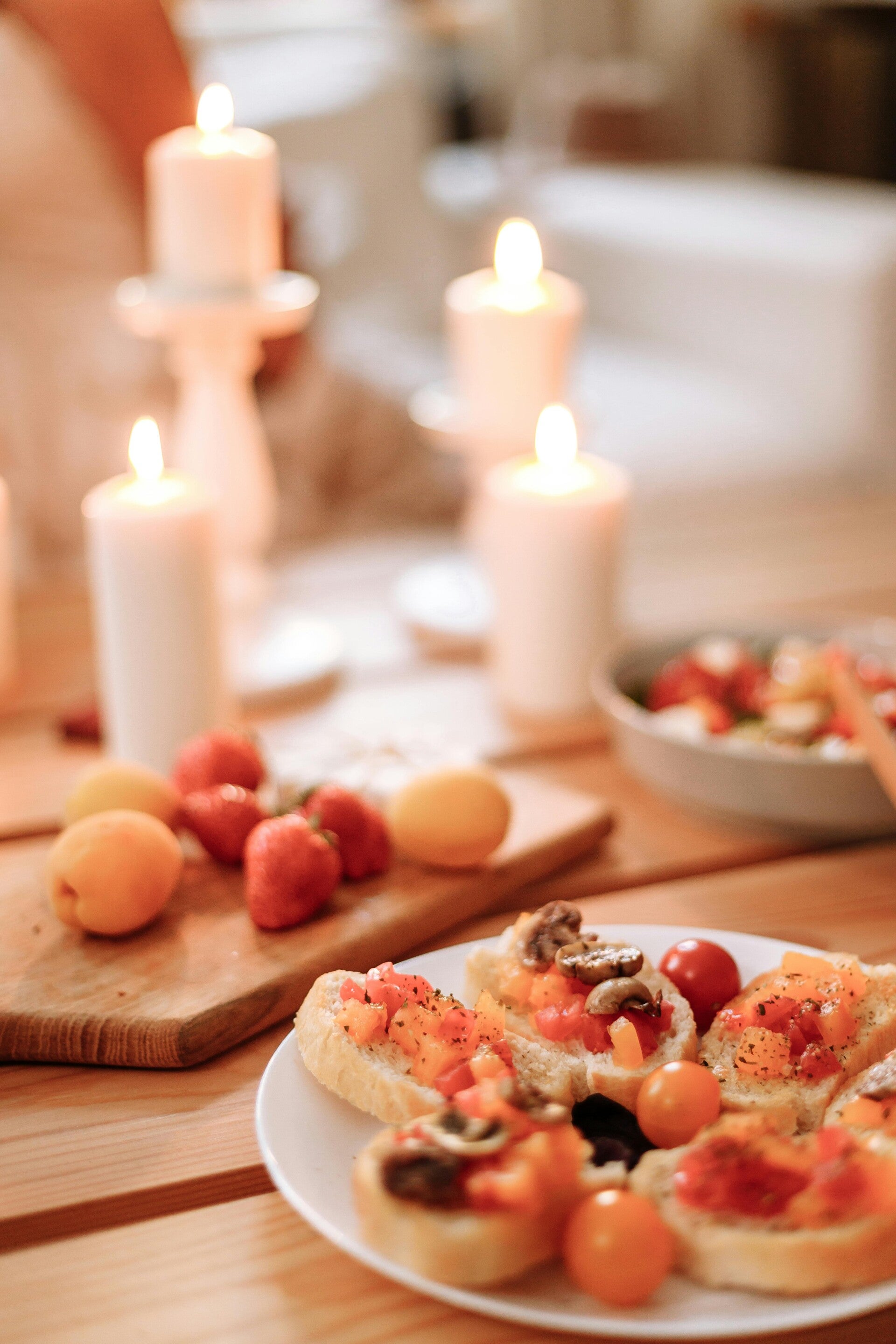 Ein Teller mit frisch zubereiteten Bruschetta-Teilchen, im Hintergrund liegen Aprikosen und Erdbeeren auf Holz.