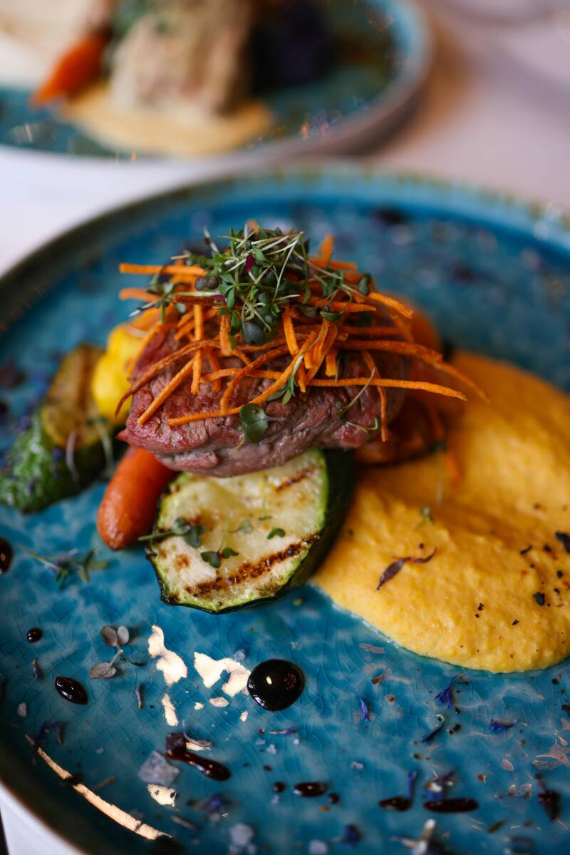Ein Fine-Dining-Gericht mit Fleisch auf einer Zucchini-Scheibe, Karottenstreifen und feinem Püree.