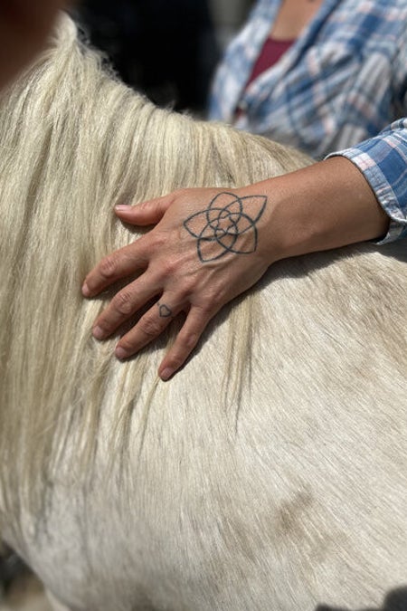 Sylvia Schlichte Hand auf weißem Schimmel Tatto mit LotusBlume auf dem Handrücken