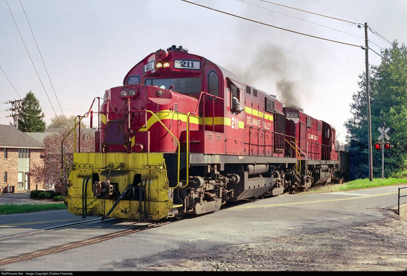a red diesel locomotive with yellow trim at a grade crossing