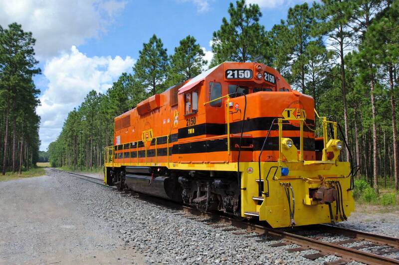 a bright orange diesel-electric locomotive in front of some trees