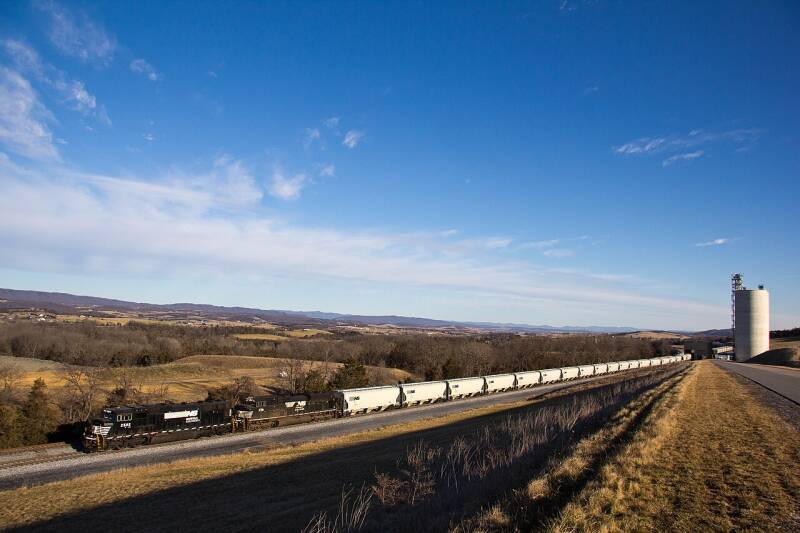 two black locomotives pull a long line of covered hopper cars 