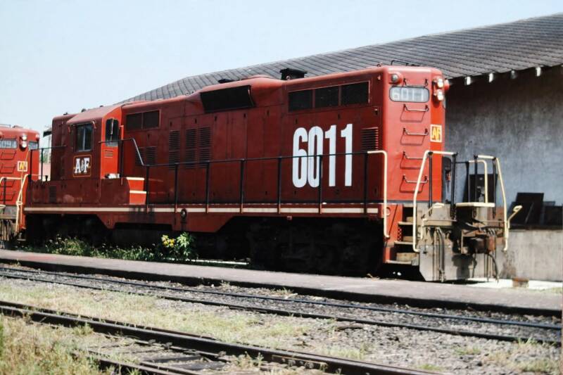 a red diesel-electric road switcher locomotive with number 6011 standing next to a trackside building.