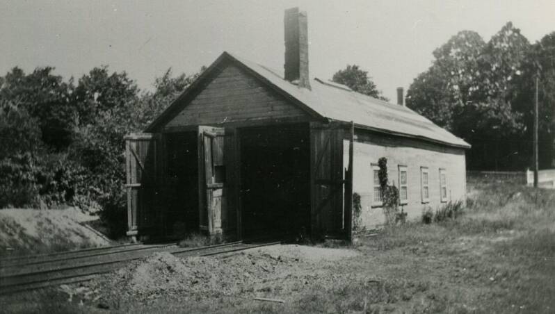 A single story building with two large doors. Train tracks lead into both doors.