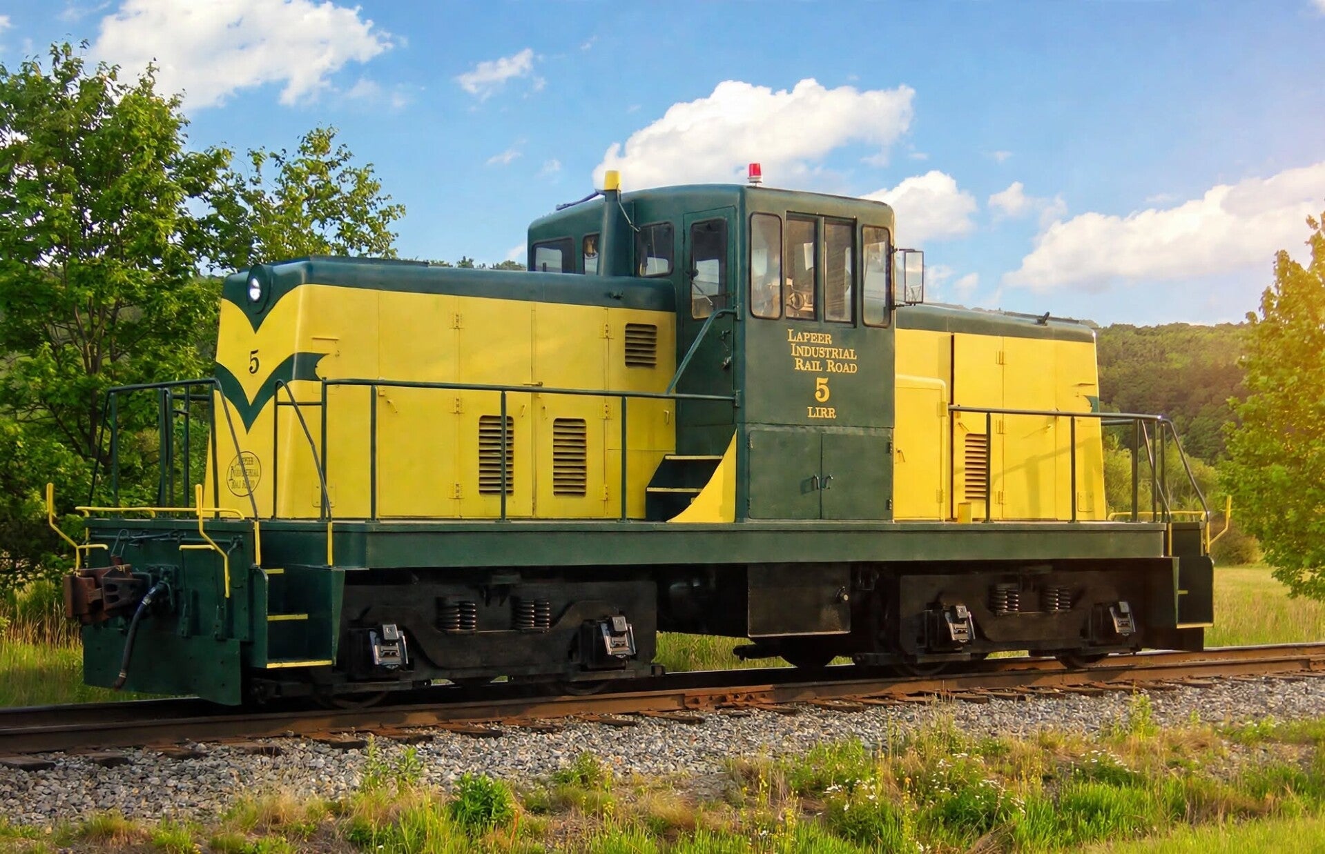 A green and yellow centercab diesel switching locomotive in a rural setting.