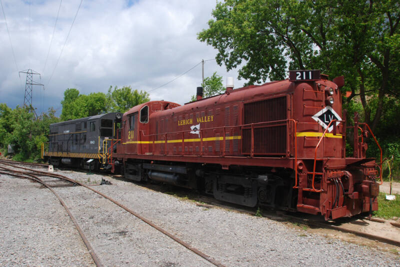 two older diesel-electric locomotives trackside next to some trees