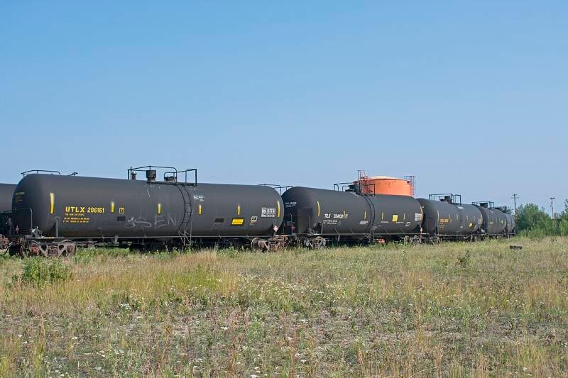A line of five gray tank cars with yellow markings.