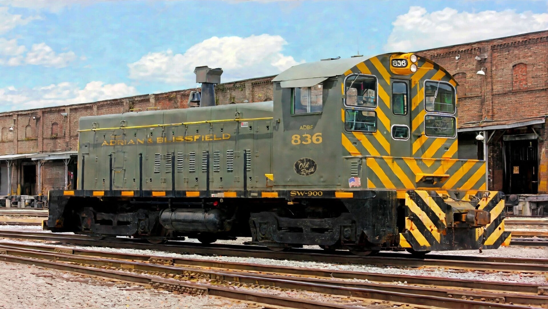 an older gray switching locomotive with yellow trim in front of warehouses