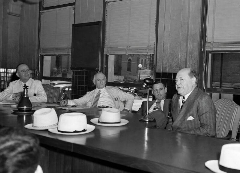 black and white photo of four well-dressed men at a large table