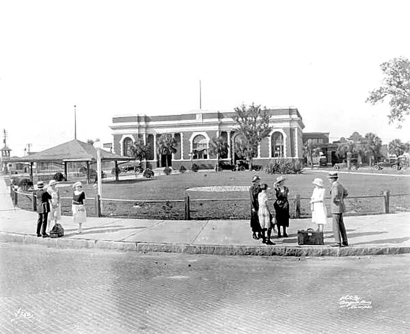 passengers standing on the curb in front of large building