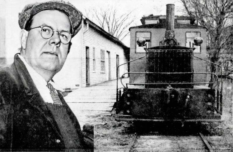 A man poses with a small locomotive at a train station.