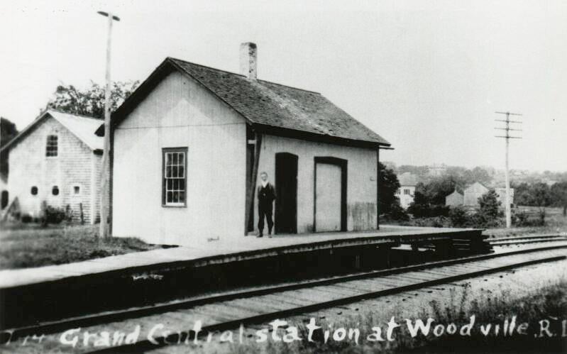 A man standing in front of a small railroad depot.