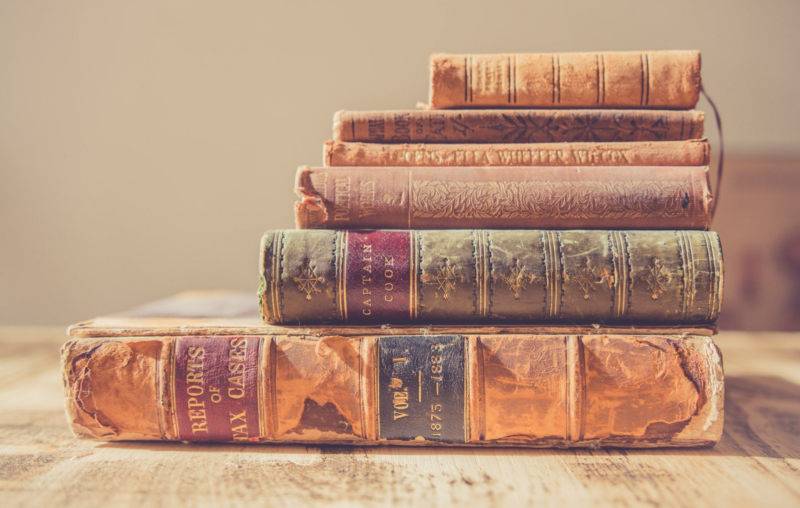 A stack of old, weathered books with faded and cracked leather covers, placed on a wooden surface
