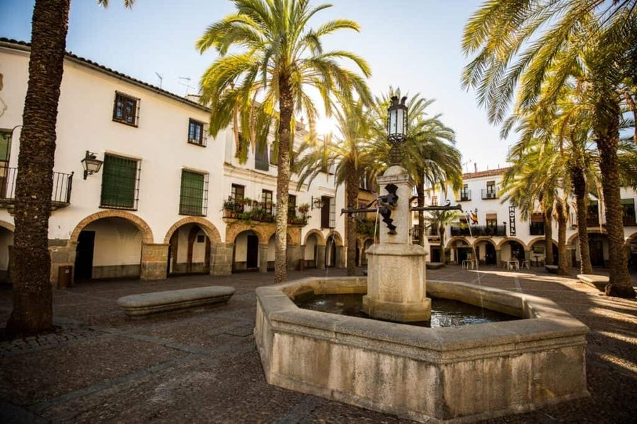 fuente de una plaza en extremadura rodeada de soportales y palmeras