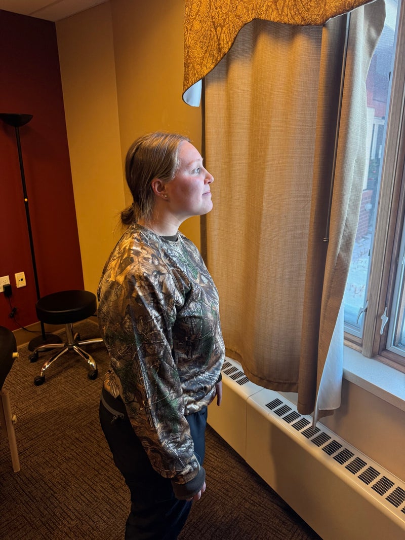 Image of a female standing by the window birdwatching with her neck extended forward like a turtle while completing chin tucks.