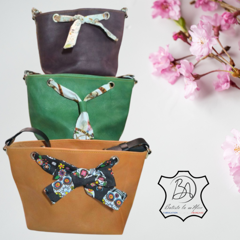 3 petits sacs cabas en cuir coloré : un violet avec un noeud en coton blanc et attrape rêve, un vert pomme avec un noeud en coton avec des attrape rêve et le 3ème sacs est orange avec un noeud en coton noir avec têtes de mort mexicaines. 