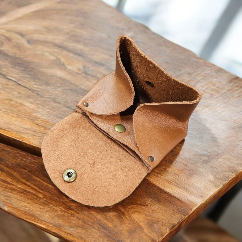 Un grand porte monnaie en cuir cognac, posé ouvert sur une table en bois massif