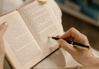Hands using a gold fountain pen to gently edit and mark patterns in an open book, illustrating Act II: The Editing process in life narrative coaching.