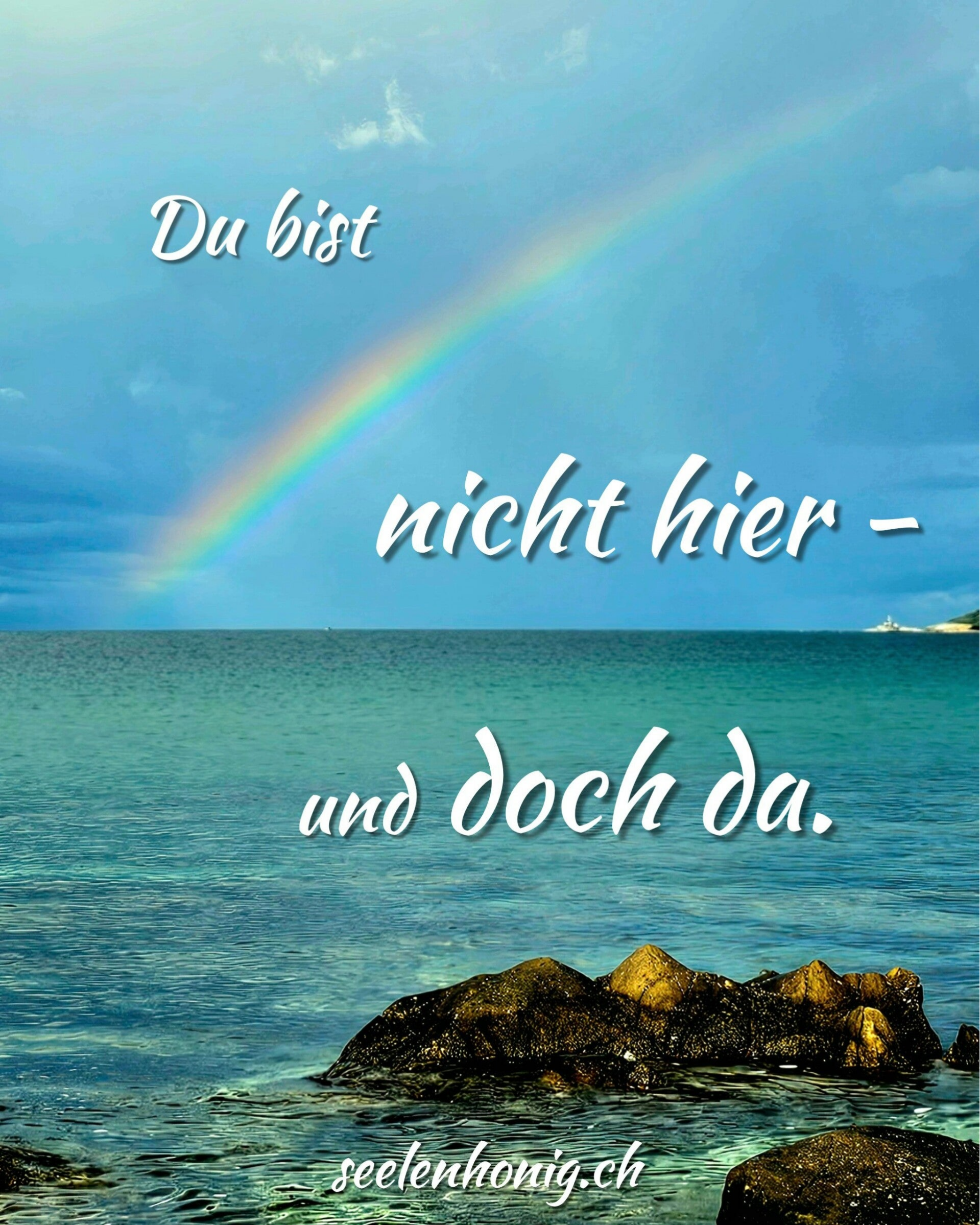 Blick über ein ruhiges Meer mit Felsen im Vordergrund, darüber ein zarter Regenbogen im hellen Himmel. Licht spiegelt sich auf Wasser und Steinen und vermittelt ein Gefühl von Nähe trotz Distanz.