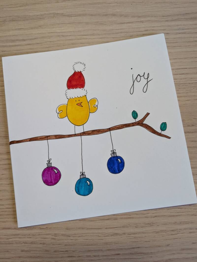 witte kaart met een kerstvogeltje op een tak waar drie kerstballen aan hangen