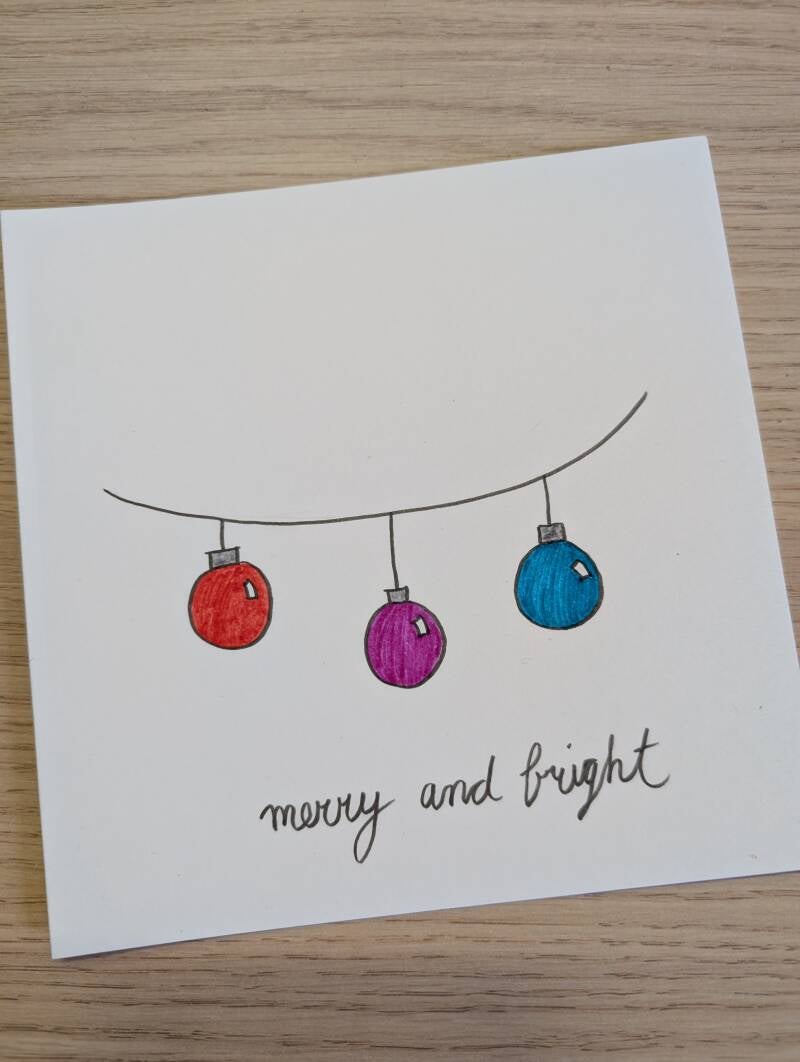 witte kaart met drie kerstballen en de tekst Merry and bright erop