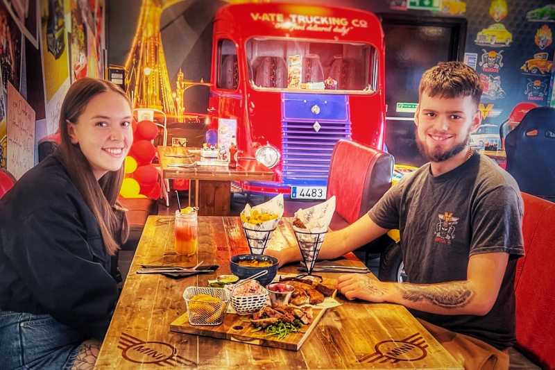 two people sat at a table enjoying a sharing platter and cocktails. Car themed tables and smiling faces