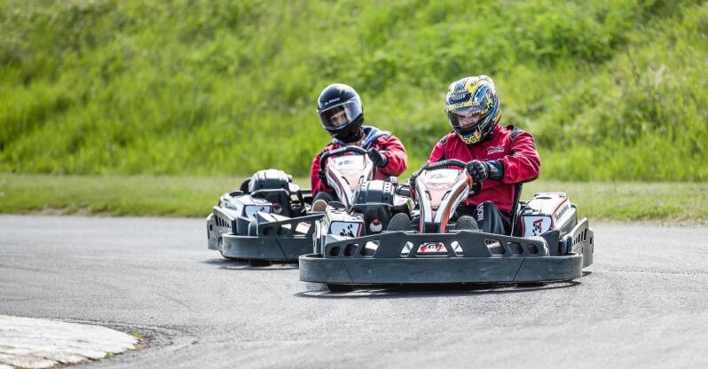 Couple in karting gear racing round a corner on go karts