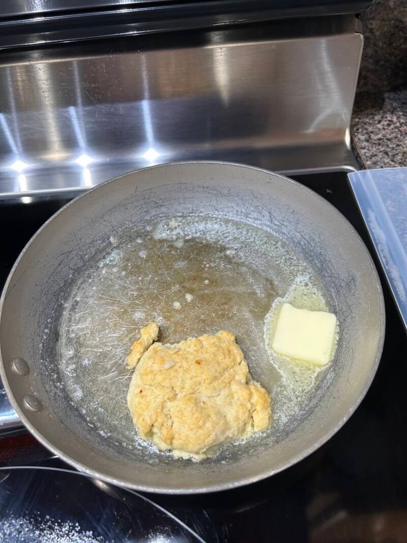 Butter melting and a biscuit in a skillet on a stove