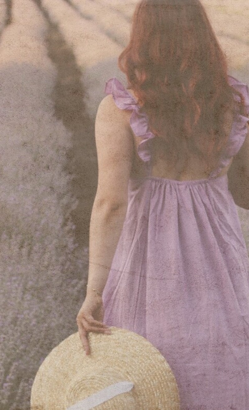 Woman in a lavender dress holding a straw hat, walking through blooming lavender fields at sunset—symbolizing renewal, choice, and quiet strength in Juliet Ellison’s clean historical romance, Letters from Willow Creek.