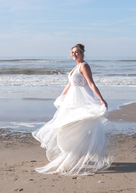 Bruid draait vrolijk op het strand met wapperende trouwjurk – bruidsfotografie op locatie